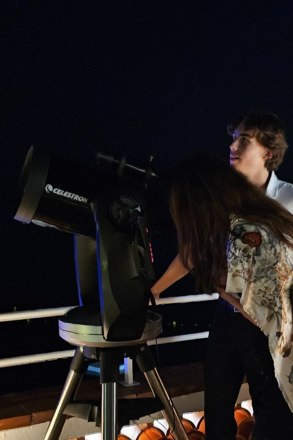 Hector accompagne une invitée au télescope, photographie recadrée pour exclure un autre visiteur
